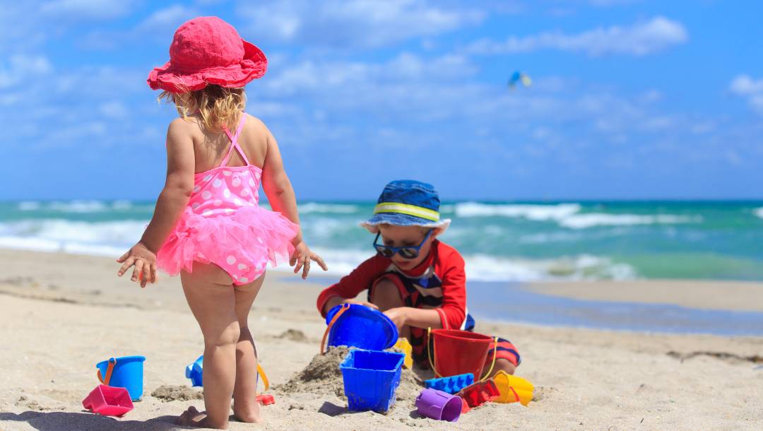 Deca u kupaćim kostimima igraju se na peščanoj plaži pored mora